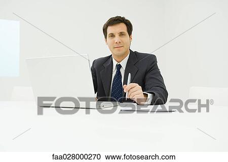 Businessman sitting at desk, using laptop computer, smiling at camera View Large Photo Image Stock Image - Businessman sitting at desk, using laptop computer, smiling at camera. Fotosearch