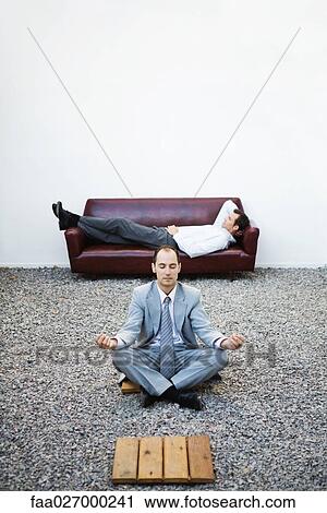 Businessman sitting in lotus position on gravel, eyes closed, colleague lying on couch in background View Large Photo Image Stock Image - Businessman sitting in lotus position on gravel, eyes closed, colleague lying on couch in background. Fotosearch