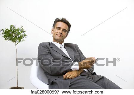 Businessman sitting, listening to MP3 player, smiling at camera View Large Photo Image Stock Photo - Businessman sitting, listening to MP3 player, smiling at camera. Fotosearch