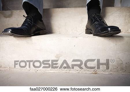 Stock Photograph - Businessman sitting on steps, cropped view of feet, low angle view. Fotosearch