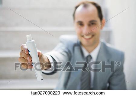Businessman sitting on steps, holding out toothpaste tube, focus on foreground View Large Photo Image Stock Photo - Businessman sitting on steps, holding out toothpaste tube, focus on foreground. Fotosearch