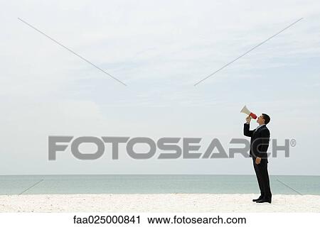 Stock Image - Businessman standing at the beach shouting into megaphone. Fotosearch