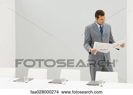 Businessman standing beside empty conference table, reading newspaper View Large Photo Image Picture - Businessman standing beside empty conference table, reading newspaper. Fotosearch