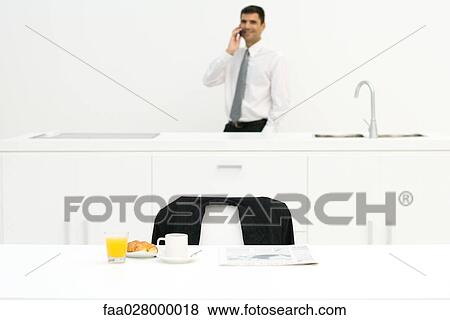 Businessman standing in kitchen, using cell phone, focus on breakfast in foreground View Large Photo Image Stock Photo - Businessman standing in kitchen, using cell phone, focus on breakfast in foreground. Fotosearch