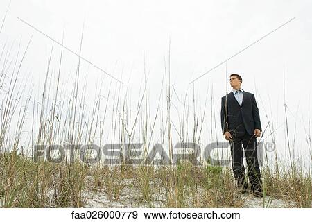 Businessman standing in tall grass, looking away, full length View Large Photo Image Stock Photo - Businessman standing in tall grass, looking away, full length. Fotosearch