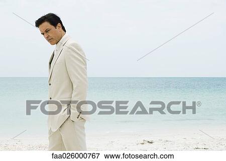 Businessman standing on beach with hands in pockets, looking down View Large Photo Image Stock Photo - Businessman standing on beach with hands in pockets, looking down. Fotosearch