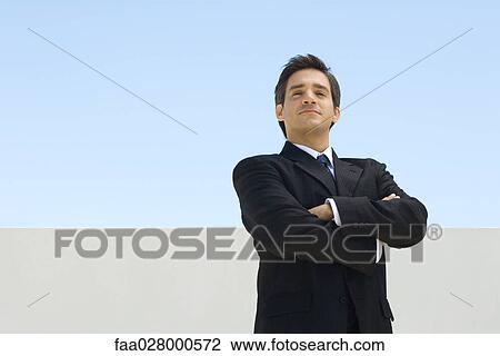 Businessman standing with arms folded, looking at camera View Large Photo Image Stock Image - Businessman standing with arms folded, looking at camera. Fotosearch