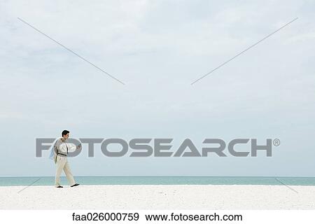Businessman walking across empty beach, looking at cell phone View Large Photo Image Stock Photo - Businessman walking across empty beach, looking at cell phone. Fotosearch