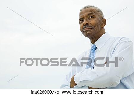 Stock Photography - Businessman with arms folded, looking away, low angle view. Fotosearch