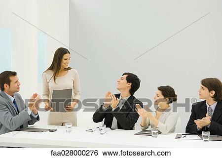 Businesswoman standing beside conference table, holding document, colleagues looking at her and clapping View Large Photo Image Stock Photograph - Businesswoman standing beside conference table, holding document, colleagues looking at her and clapping. Fotosearch