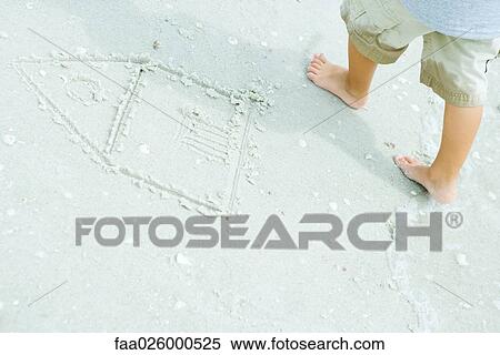 Stock Photography - Child at the beach, standing next to drawing of house in sand, cropped view. Fotosearch