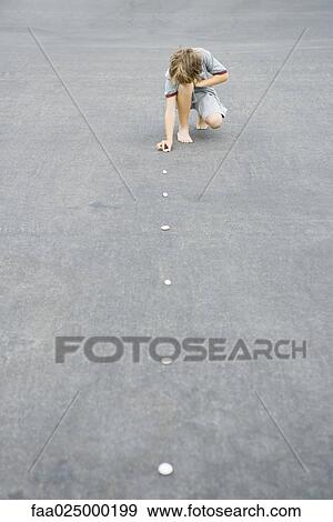 Child crouching on the ground, lining up pebbles, full length View Large Photo Image Stock Photo - Child crouching on the ground, lining up pebbles, full length. Fotosearch