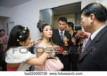Stock Photograph - Chinese wedding, bridesmaid putting necklace on bride while others watch. Fotosearch