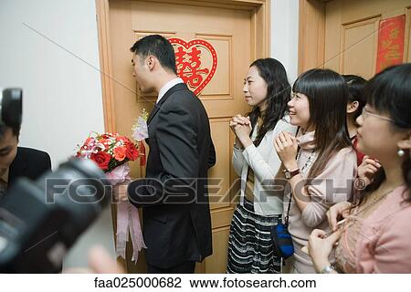 Stock Image - Chinese wedding, groom holding bouquet and knocking on bride's door while bride's friends watch. Fotosearch