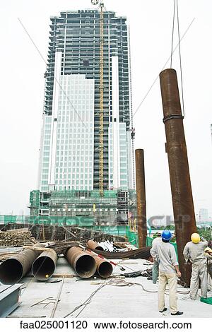 Construction workers at construction site, pipe being lifted into air View Large Photo Image Stock Image - Construction workers at construction site, pipe being lifted into air. Fotosearch