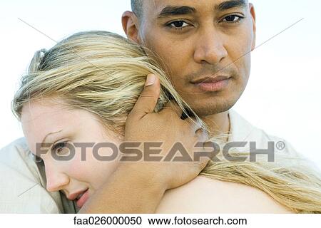 Stock Image - Couple embracing, man looking at camera, close-up. Fotosearch