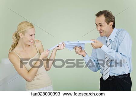 Stock Image - Couple fighting over baby clothing, smiling at each other. Fotosearch