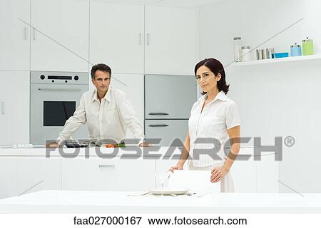 Couple in kitchen, man preparing meal, woman setting table View Large Photo Image Stock Photo - Couple in kitchen, man preparing meal, woman setting table. Fotosearch