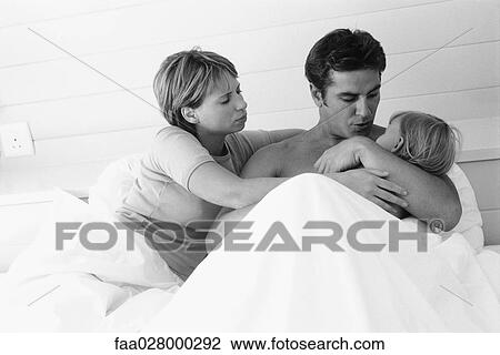 Couple lying in bed, man holding child in arms View Large Photo Image Stock Image - Couple lying in bed, man holding child in arms. Fotosearch