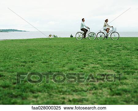 Stock Photography - Couple riding bicycles at water's edge, mid-distance. Fotosearch