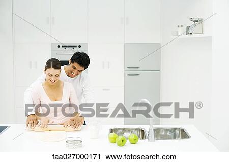 Stock Image - Couple rolling out dough with rolling pin together, both smiling. Fotosearch