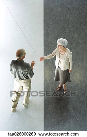 Stock Photo - Couple standing on divided black and white floor, woman holding hand out in greeting, high angle view. Fotosearch
