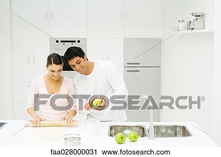 Couple standing together at kitchen counter, woman rolling out dough, man peeling apple View Large Photo Image Stock Image - Couple standing together at kitchen counter, woman rolling out dough, man peeling apple. Fotosearch