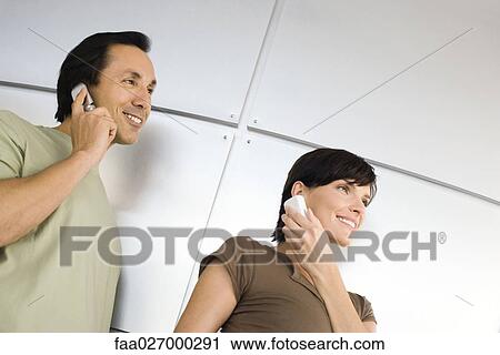 Couple using cell phones, smiling, looking away, low angle view View Large Photo Image Stock Image - Couple using cell phones, smiling, looking away, low angle view. Fotosearch