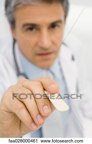Doctor holding tongue depressor toward camera, close-up View Large Photo Image Stock Image - Doctor holding tongue depressor toward camera, close-up. Fotosearch