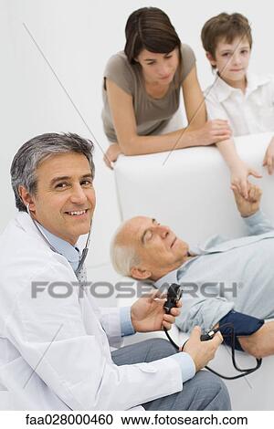Doctor measuring patient's blood pressure, smiling over shoulder at camera, patient's family in background View Large Photo Image Stock Image - Doctor measuring patient's blood pressure, smiling over shoulder at camera, patient's family in background. Fotosearch