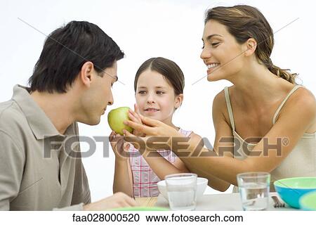 Family of healthy eaters, mother and daughter holding apple toward father View Large Photo Image Stock Image - Family of healthy eaters, mother and daughter holding apple toward father. Fotosearch