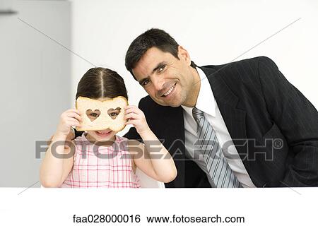 Father and daughter sitting side by side, girl looking through slice of bread with heart-shaped holes, both smiling at camera View Large Photo Image Stock Photograph - Father and daughter sitting side by side, girl looking through slice of bread with heart-shaped holes, both smiling at camera. Fotosearch