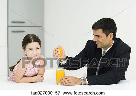 Father and daughter sitting together at table, man squeezing orange juice into glass, girl smiling at camera View Large Photo Image Stock Photo - Father and daughter sitting together at table, man squeezing orange juice into glass, girl smiling at camera. Fotosearch