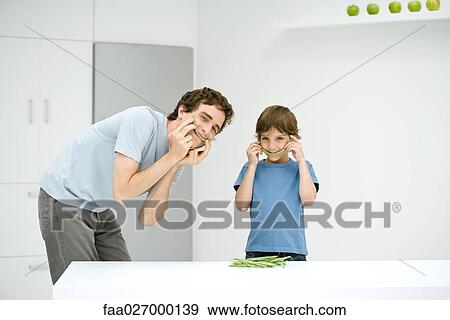 Father and son holding green beans up to their faces, smiling at camera View Large Photo Image Stock Photo - Father and son holding green beans up to their faces, smiling at camera. Fotosearch