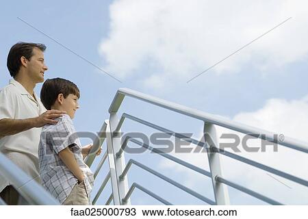 Father and son standing by railing looking at sky, low angle view View Large Photo Image Stock Image - Father and son standing by railing looking at sky, low angle view. Fotosearch