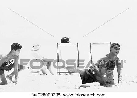 Stock Photography - Father and two teen sons roughhousing on beach. Fotosearch