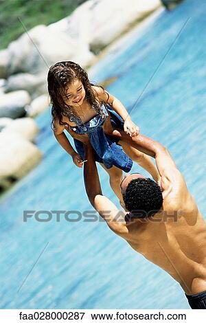 Stock Photo - Father lifting daughter in the air at the beach, rear view. Fotosearch