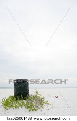 Stock Photo - Garbage can on beach, litter lying on the ground nearby. Fotosearch