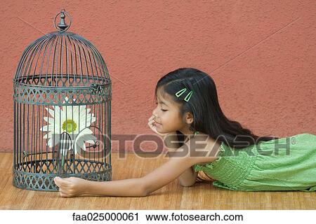 Stock Image - Girl opening up birdcage, looking at flower. Fotosearch