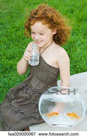 Girl sitting next to goldfish bowl, drinking water View Large Photo Image Stock Photo - Girl sitting next to goldfish bowl, drinking water. Fotosearch