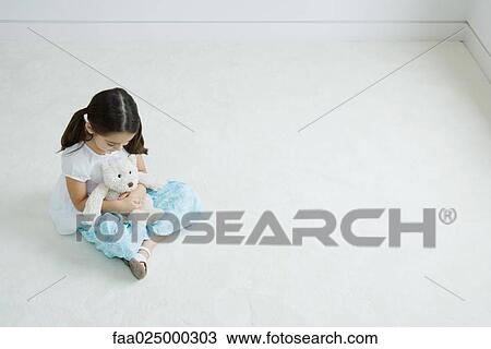 Girl sitting on the ground holding teddy bear on lap, high angle view View Large Photo Image Stock Image - Girl sitting on the ground holding teddy bear on lap, high angle view. Fotosearch