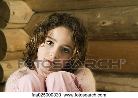 Stock Image - Girl sitting with knees up, looking at camera. Fotosearch