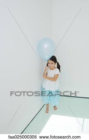 Girl standing in corner holding balloon, looking up at camera View Large Photo Image Stock Photography - Girl standing in corner holding balloon, looking up at camera. Fotosearch