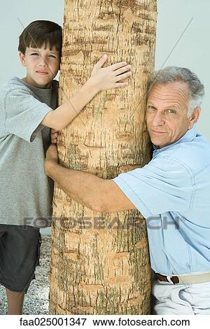 Grandfather and grandson hugging tree trunk, both looking at camera View Large Photo Image Stock Photo - Grandfather and grandson hugging tree trunk, both looking at camera. Fotosearch