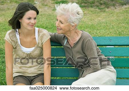 Grandmother and teenage granddaughter sitting together on bench, both smiling View Large Photo Image Picture - Grandmother and teenage granddaughter sitting together on bench, both smiling. Fotosearch