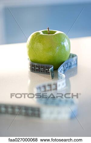 Stock Photo - Green apple with tape measure around it, close-up. Fotosearch