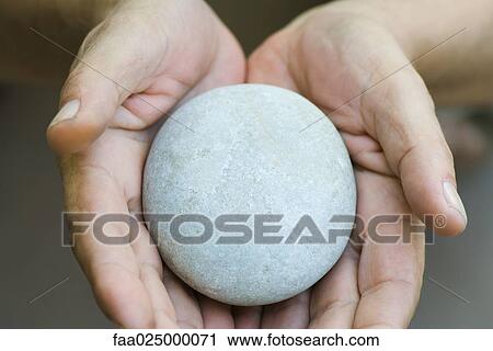 Stock Image - Hands holding out round pebble. Fotosearch