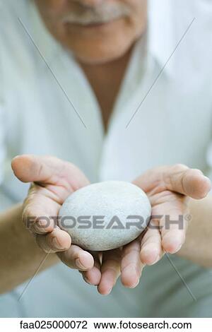 Stock Image - Hands holding out round pebble. Fotosearch