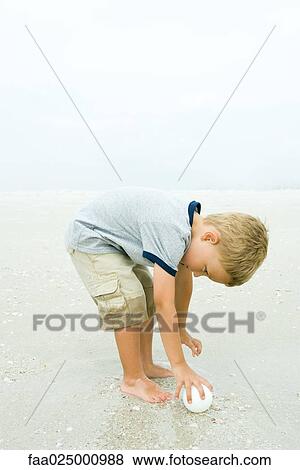 Little boy bending over to pick up ball on beach, full length View Large Photo Image Stock Photo - Little boy bending over to pick up ball on beach, full length. Fotosearch