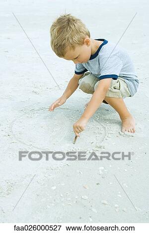 Stock Photo - Little boy crouching at the beach, drawing in sand with stick. Fotosearch